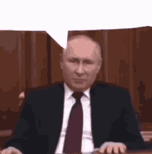 a man in a suit and tie is sitting at a desk with a speech bubble .