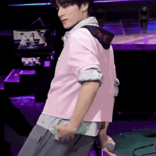 a man in a pink shirt and gray pants is standing on a stage holding a microphone .