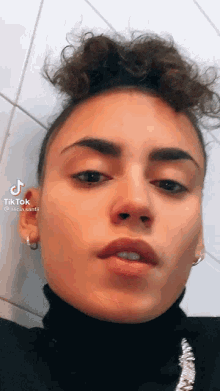 a woman with curly hair is wearing a black turtleneck and earrings and looking at the camera .