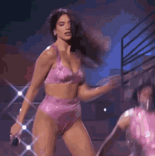a woman in a pink bikini is dancing on a stage with a microphone in her hand .