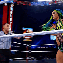 a woman with green hair is standing in a wrestling ring talking to a referee .