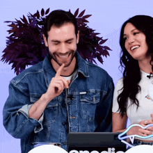 a man in a denim jacket laughs next to a woman in a white shirt