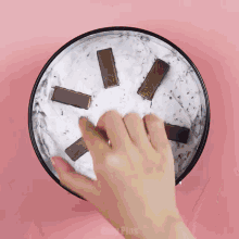 a person 's hand reaches into a bowl of ice cream with kitkat bars on top