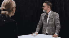 a man in a plaid jacket and tie talks to a woman