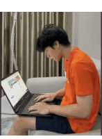 a man in an orange shirt is typing on a laptop computer