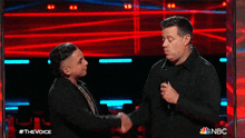 a man and a woman shaking hands on a stage with a microphone .