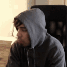 a man wearing a gray hoodie is sitting in a chair