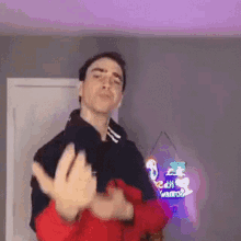 a man in a black hoodie and red jacket is making a funny face .
