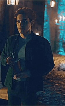 a man in a green jacket is standing in a dark room holding a cup of coffee .