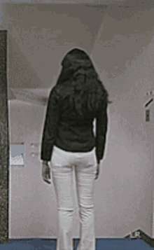 a woman standing in front of a door wearing white pants and a black shirt