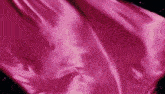 a pink satin fabric is waving in the wind on a black background .