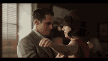 a man in a suit and tie is dancing with a woman in a red dress and hat