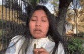 a woman is sitting in front of a fence with her eyes closed and holding a piece of wood in her hand .
