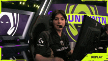 a man wearing headphones and a logitech shirt sits in front of a computer monitor