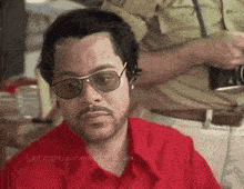 a man wearing sunglasses and a red shirt says " last night someone came and killed me "