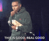 a man in a green hoodie is eating popcorn and holding a microphone with the words " this is good real good " below him