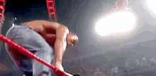 a man is kneeling down in a wrestling ring while holding onto a red rope .