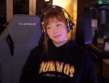 a woman wearing headphones and a hummus sweatshirt sits in front of a querus chair