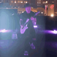 a man playing a guitar on a stage with purple lights behind him