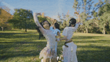 three women are dancing in a park with their arms outstretched