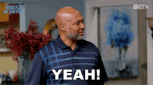 a man in a blue shirt says yeah in front of a picture of flowers