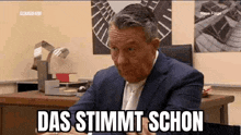 a man in a suit and tie is sitting at a desk in an office with a clock on the wall .