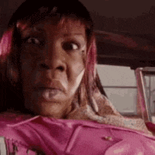 a woman with pink hair is sitting in a car with a pink jacket on .
