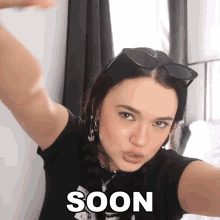 a woman wearing sunglasses takes a selfie with the word soon written on the bottom