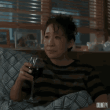 a woman is drinking a glass of wine while laying on a bed .