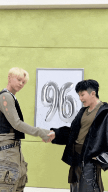two men shaking hands in front of a poster with the number 96