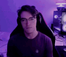 a young man wearing glasses and headphones is sitting in a gaming chair in front of a computer .