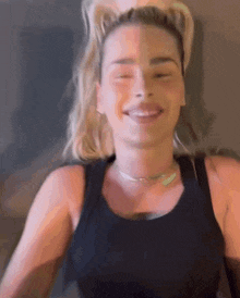 a woman wearing a black tank top and a necklace smiles with her eyes closed