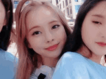 three young women are posing for a picture together . one of the girls is wearing a blue shirt .