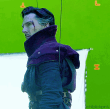 a man in a purple coat is standing in front of a green screen with the letters l and i on it
