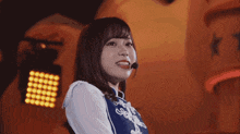 a woman wearing a microphone and a blue top is smiling