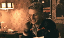 a man wearing a fila jacket is smiling while talking on a cell phone