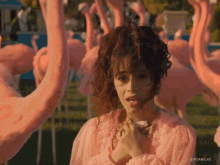 a woman in a pink dress stands in front of a flock of pink flamingos