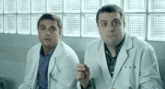 two men in lab coats are sitting next to each other in front of a window