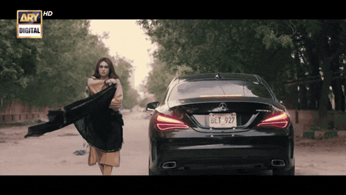 a woman stands in front of a black mercedes with a license plate that says bet 927
