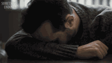 a man rests his head on a table with something undone written above him