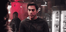 a man in a hoodie is standing in a bar talking to another man .
