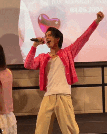 a man in a pink cardigan is singing into a microphone with his arms outstretched