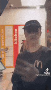 a man wearing a black mcdonald 's shirt is standing in front of a kitchen sign