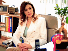 a woman in a white jacket sits in a chair with her hands folded