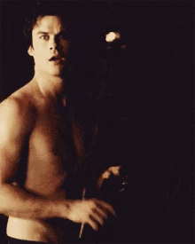 a shirtless man is standing in a dark room in front of a lamp .