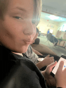 a young boy blowing a kiss while holding a cell phone