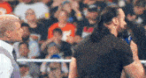 two men are standing next to each other in a wrestling ring and one of them is holding a microphone .
