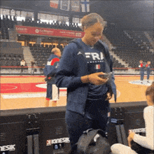 a woman wearing a shirt that says fri is looking at her phone .