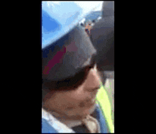a man wearing a blue hard hat and sunglasses is standing in front of a crowd .
