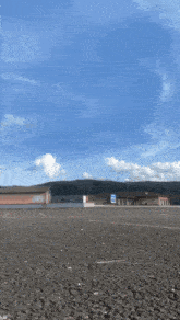 an empty parking lot with a building in the background and a blue sky with clouds